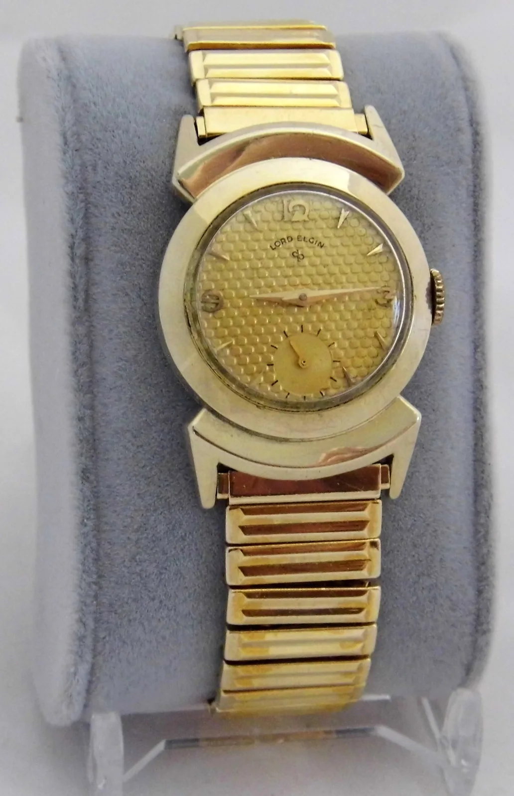 Vintage Lord Elgin men's wristwatch with a gold-colored case, champagne dial and expanding gold-colored bracelet on a display stand