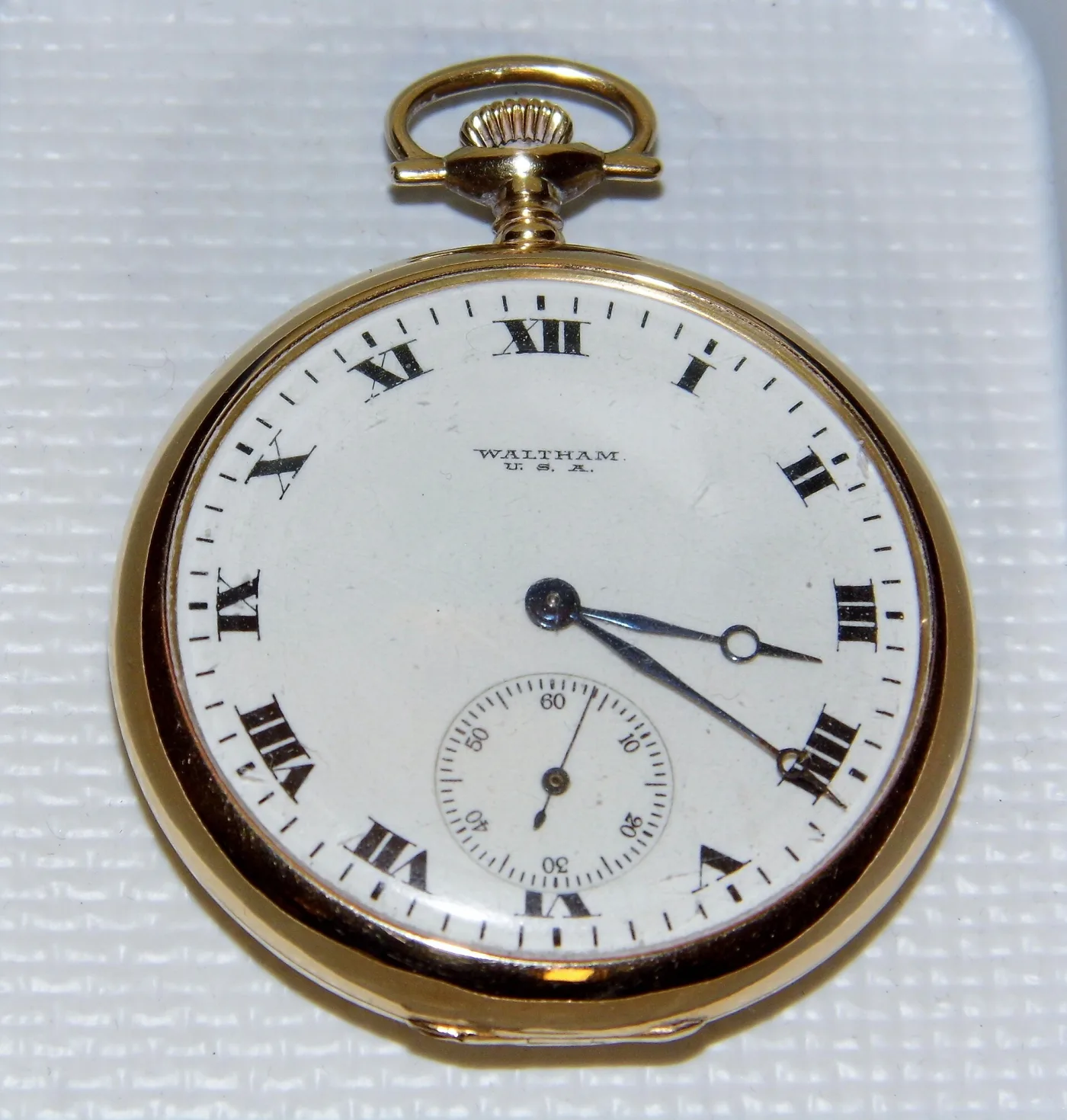 Open-face Waltham pocket watch with a white enamel dial, black Roman numerals, a small seconds dial and a yellow 14 kt gold case and bow