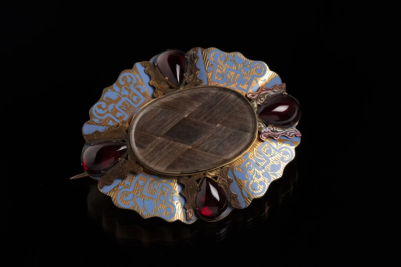 Oval mourning brooch with a central glazed panel over pale woven hair, held in a scalloped gilt frame with a long pin stem across the back