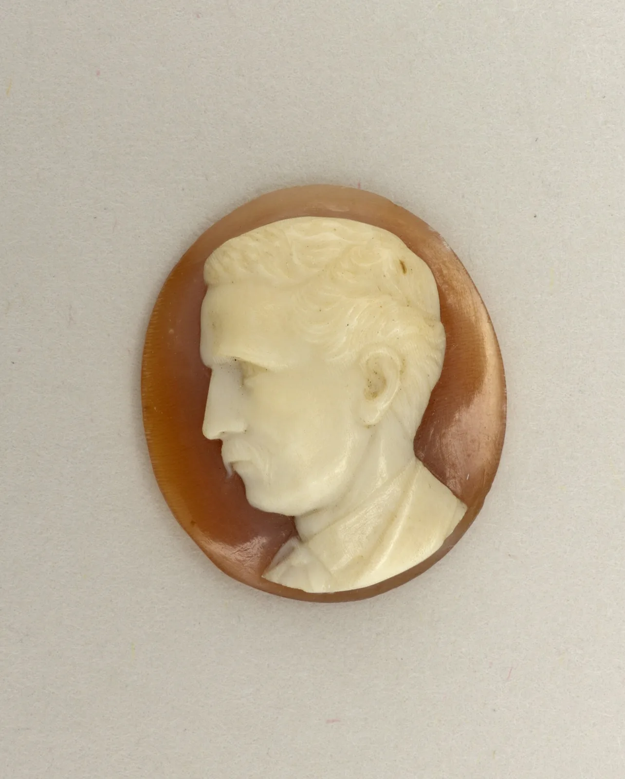 Unmounted oval shell cameo of a man with short hair and a moustache in left-facing profile, cream relief on an orange-brown ground