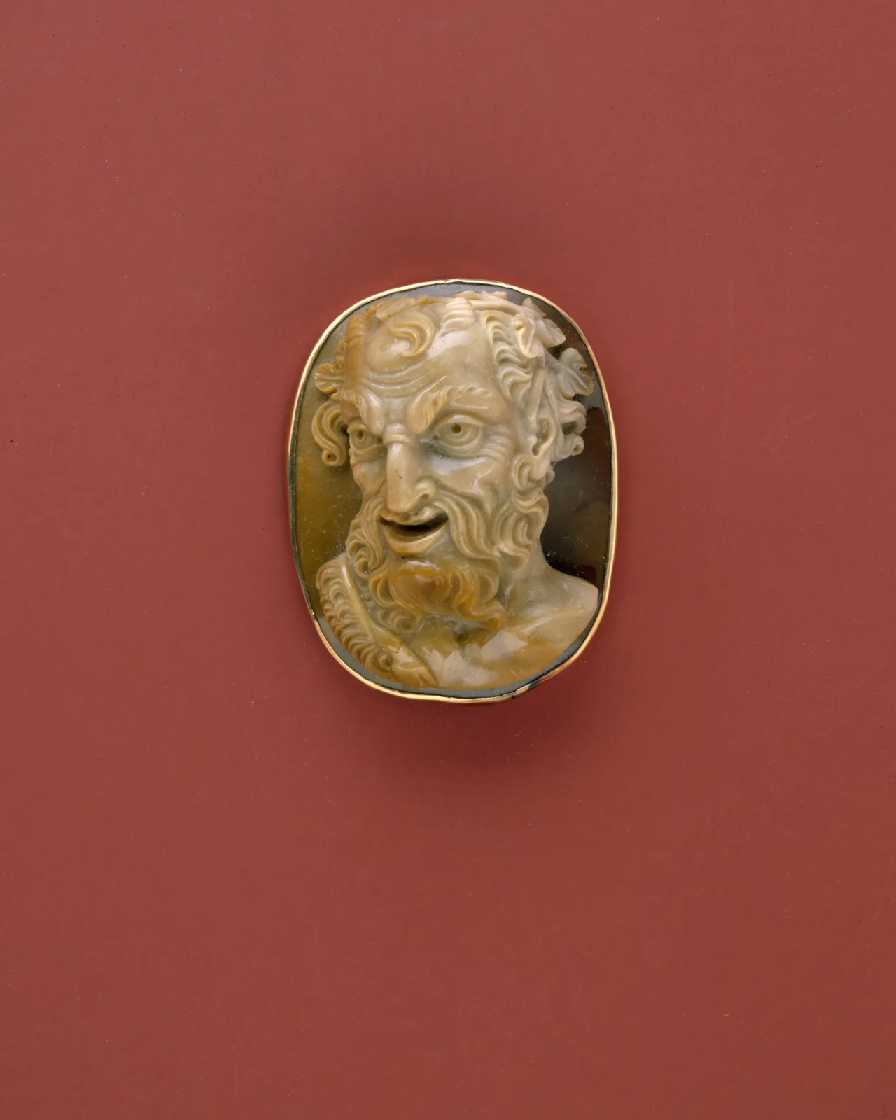 Brown and cream sardonyx cameo of a grinning satyr with curling hair and a full beard, turned three-quarters toward the viewer, in a plain gold mount