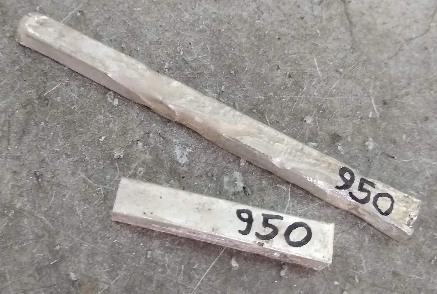 Two bars of silver on a concrete surface, each hand-labelled 950 in black marker