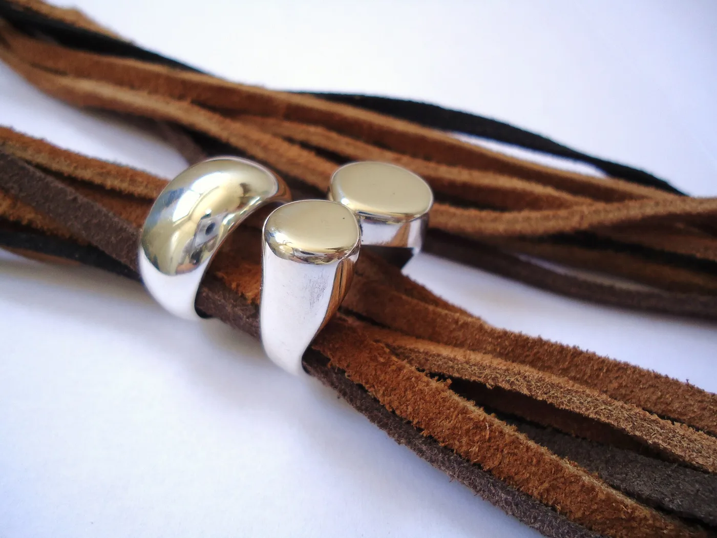 Two polished silver rings with rounded tops resting on strips of brown leather